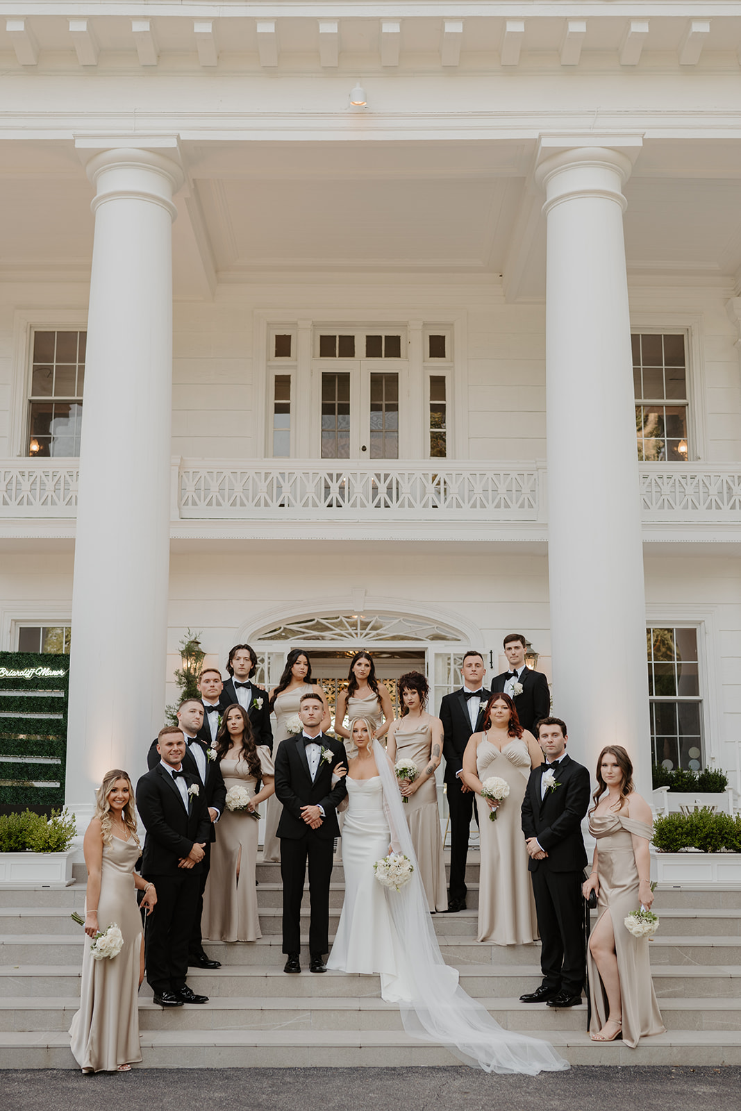 Formal portrait of the wedding party posing on the steps of the grand white manor.